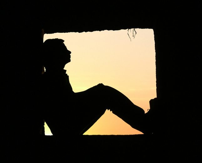 silhouette of a man sitting on a window at sunset